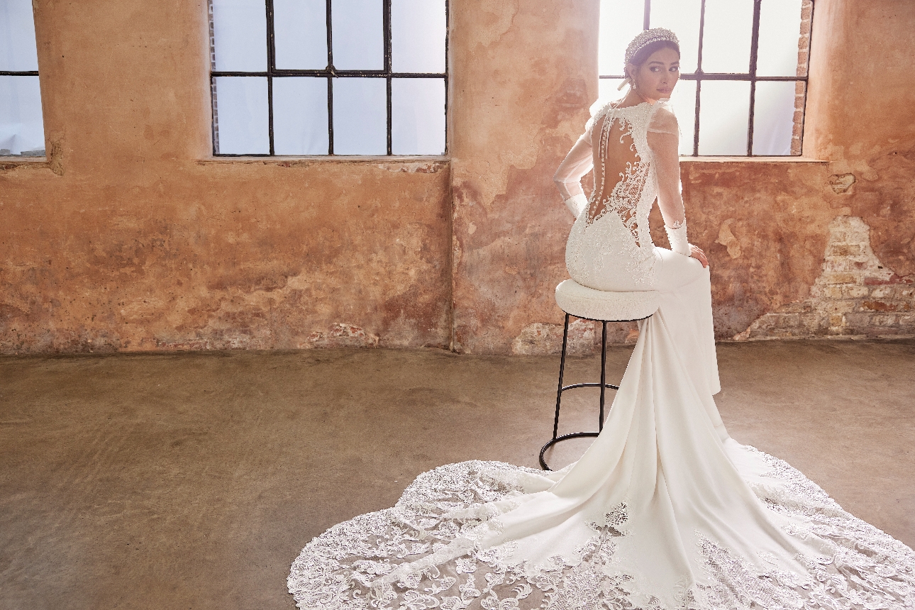 model sat on chair in white fishtail gown wiith lace brocade details on back and sleeves and train