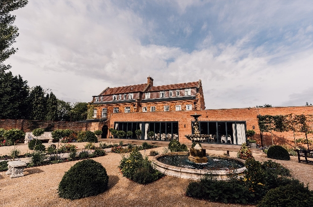 The exterior of a grand house with a wall of windows and manicured gardens