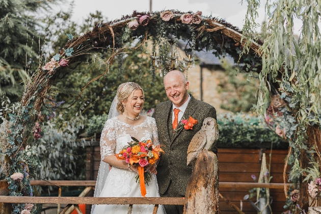 A bride and groom standing underneath an arch with an owl