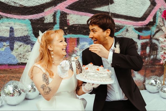 retro styled wedding couple in front of graffiti wall eating cake 
