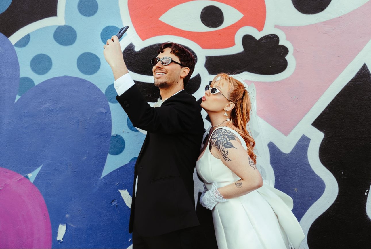 retro styled wedding couple in front of graffiti wall taking selfie