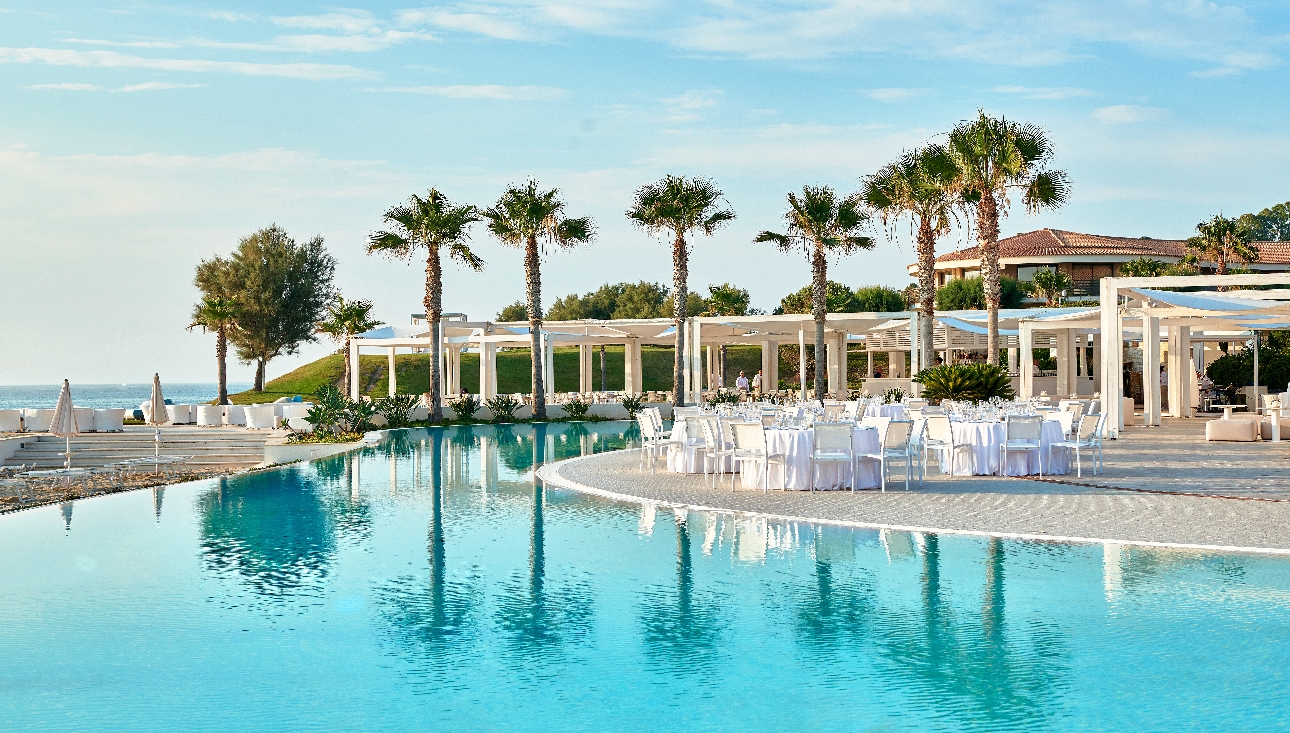 An outdoor swimming pool surrounded by seating and palm trees